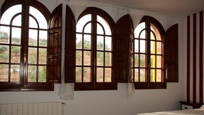 Un dormitorio con una cama grande, un radiador y tres ventanales con cortinas.