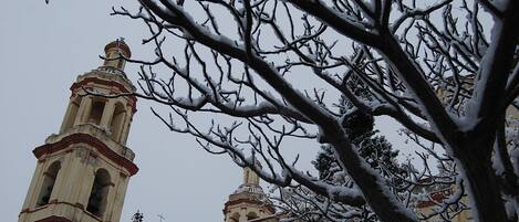Une église dotée d’un clocher, avec des branches enneigées au premier plan.