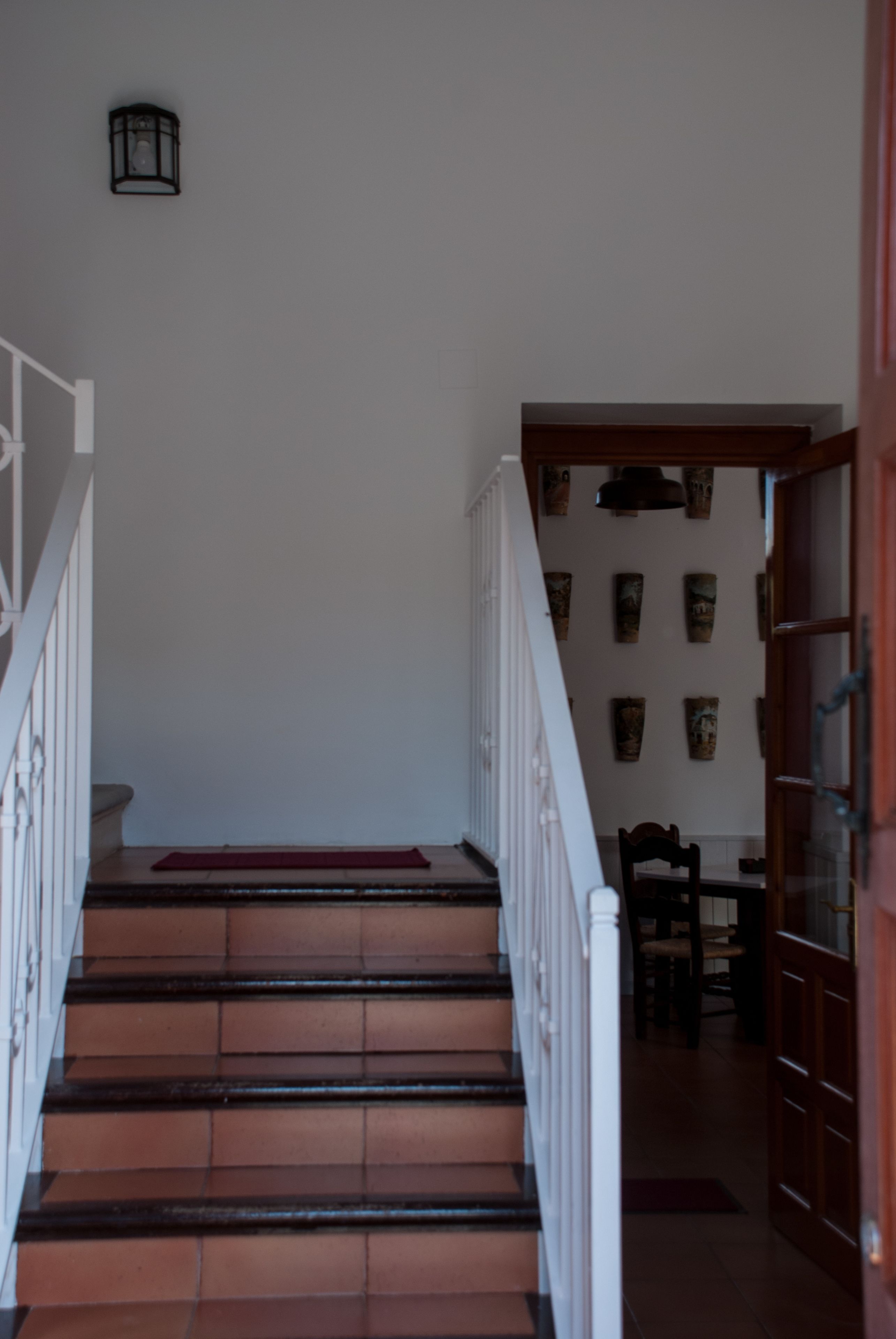 Un escalier recouvert d’une moquette rouge, avec une rampe blanche et un mur orné de tableaux encadrés.