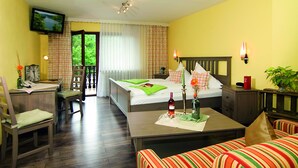 A hotel room with a bed, a desk, a chair, a television, and a view of greenery outside.