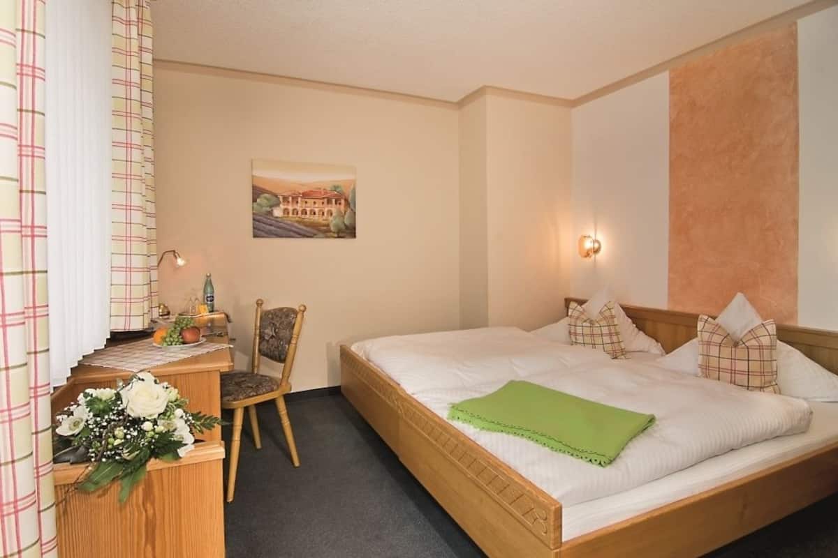 Une chambre d’hôtel avec un lit, un bureau et une chaise, une lampe fixée au mur et un tableau.