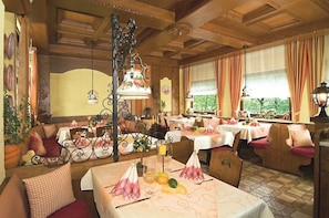 A restaurant with wooden interiors, tables set with tablecloths, and a view of greenery outside. - Gasthof Zum Spessart (Mespelbrunn)