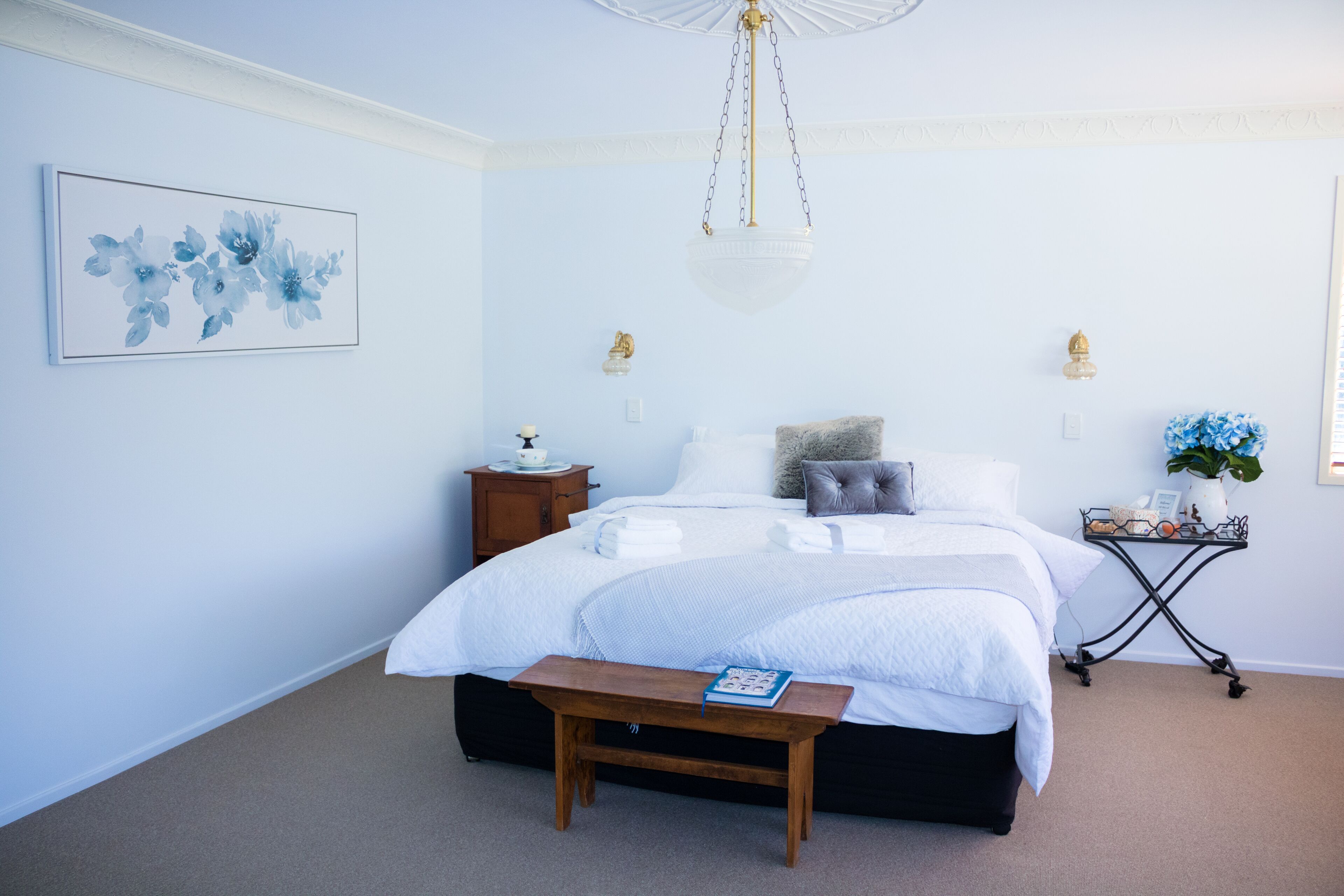 A bedroom with a large bed, bedside tables, a hanging light fixture, and a framed floral artwork on the wall.