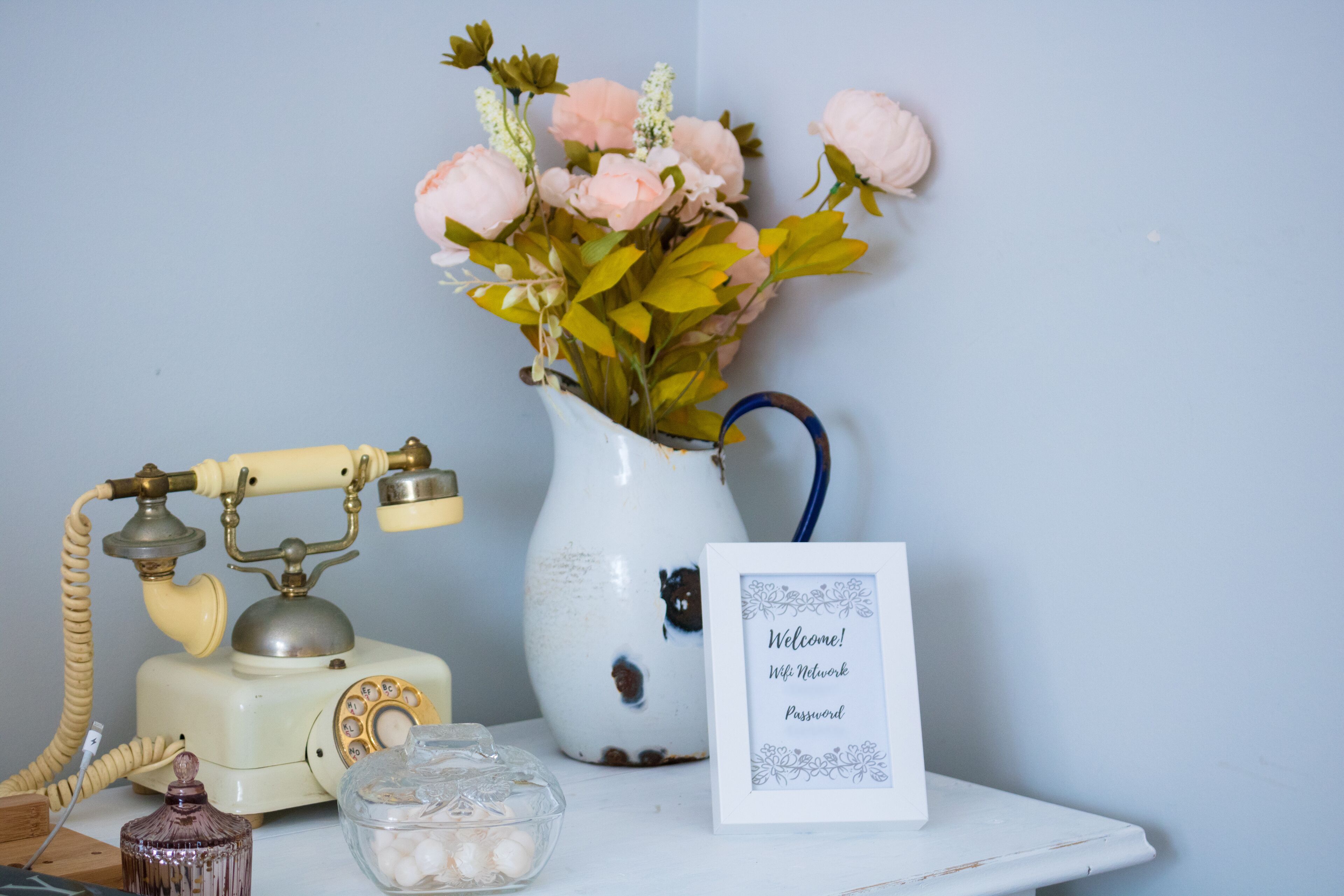 A vintage telephone, a vase with flowers, a glass jar, and a welcome sign.