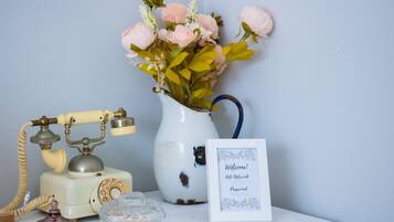 A vintage telephone, a vase with flowers, a glass jar, and a welcome sign.