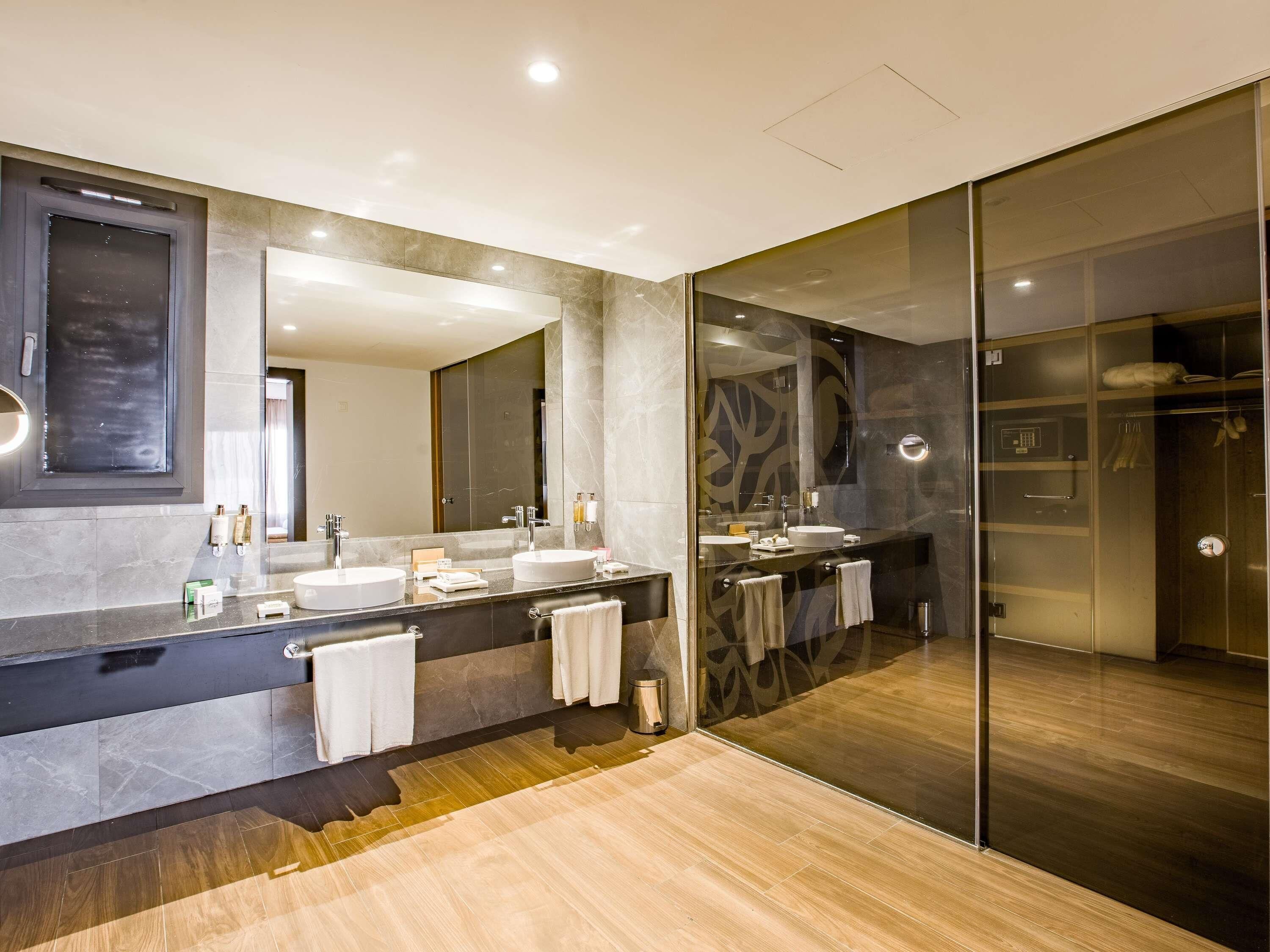 A modern bathroom with two sinks, a large mirror, and a walk-in shower.