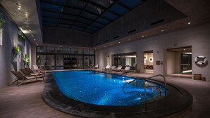 Piscina interna com espreguiçadeiras e teto de vidro.