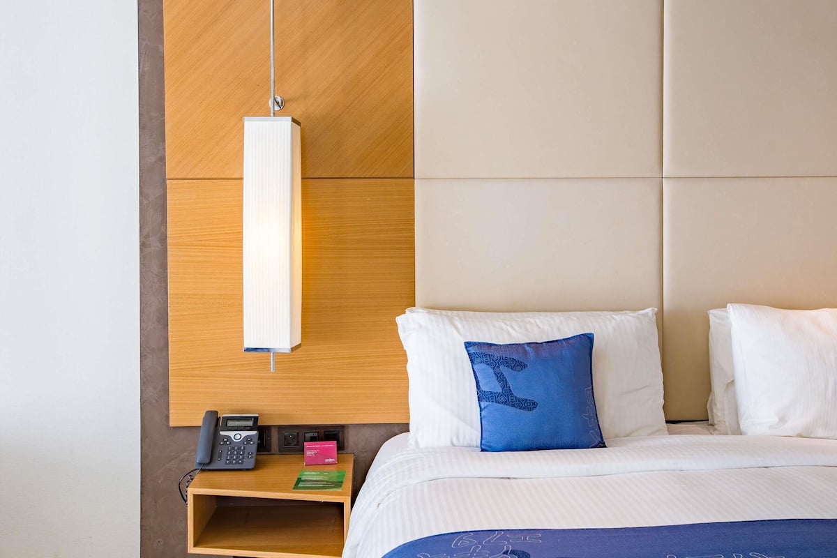 Une chambre d’hôtel avec un lit, une table de chevet avec un téléphone, une lampe et un oreiller bleu.
