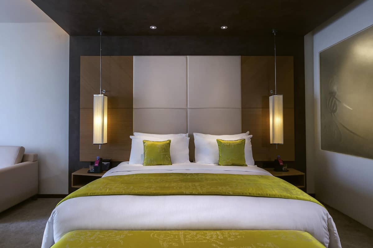 Une chambre d’hôtel moderne avec un grand lit, deux tables de chevet, une petite table et un grand tableau au mur.