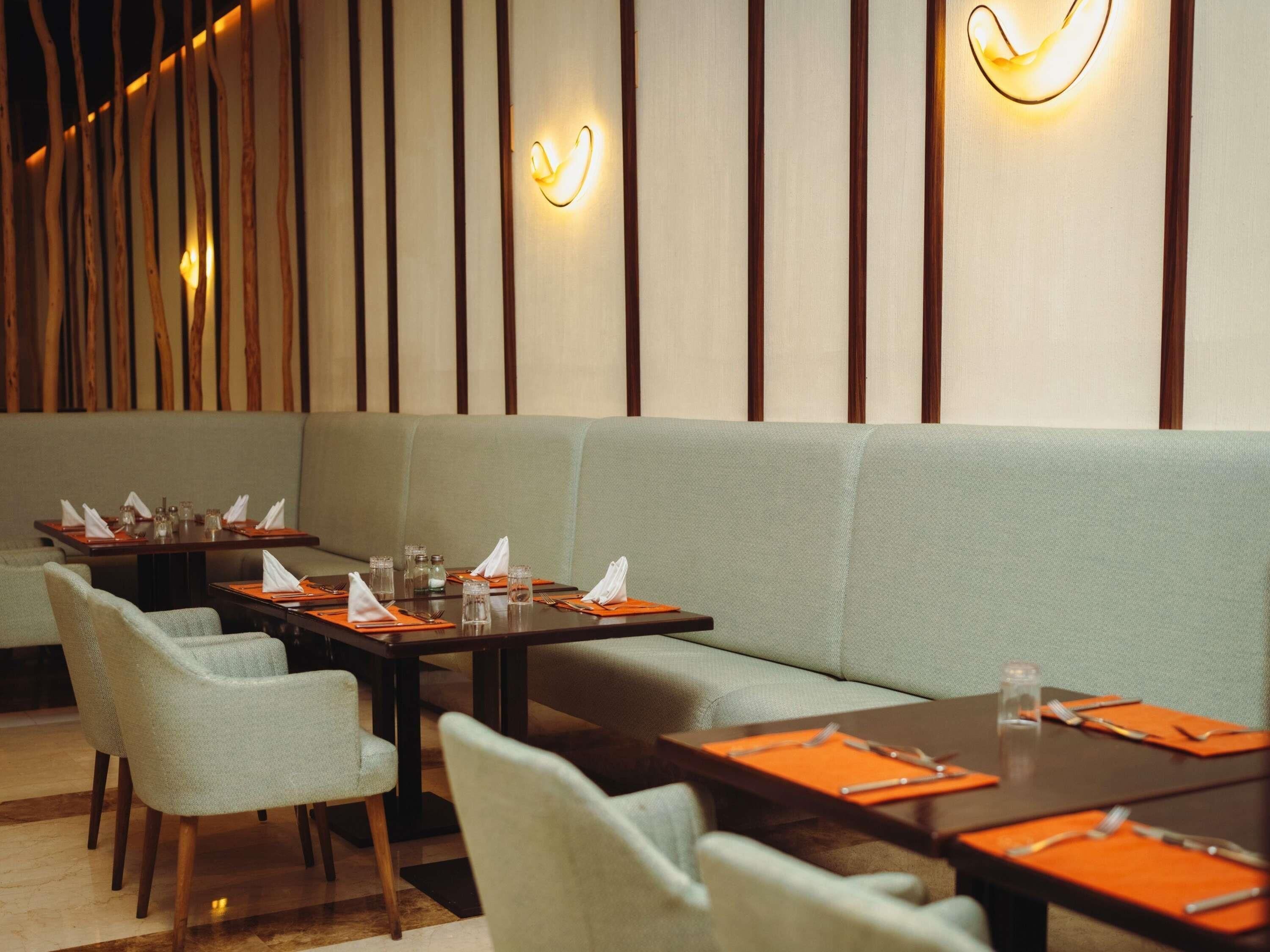 A restaurant with tables set for dining, a sofa, and wall-mounted lighting.