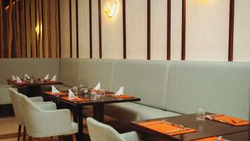 A restaurant with tables set for dining, a sofa, and wall-mounted lighting.