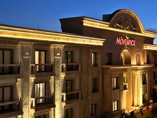 Un hotel de varios pisos con un diseño arquitectónico clásico, que cuenta con balcones y una entrada destacada con un cartel luminoso.