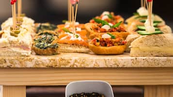 A variety of appetizers on a wooden board, including items with toothpicks and a small bowl of black pepper.