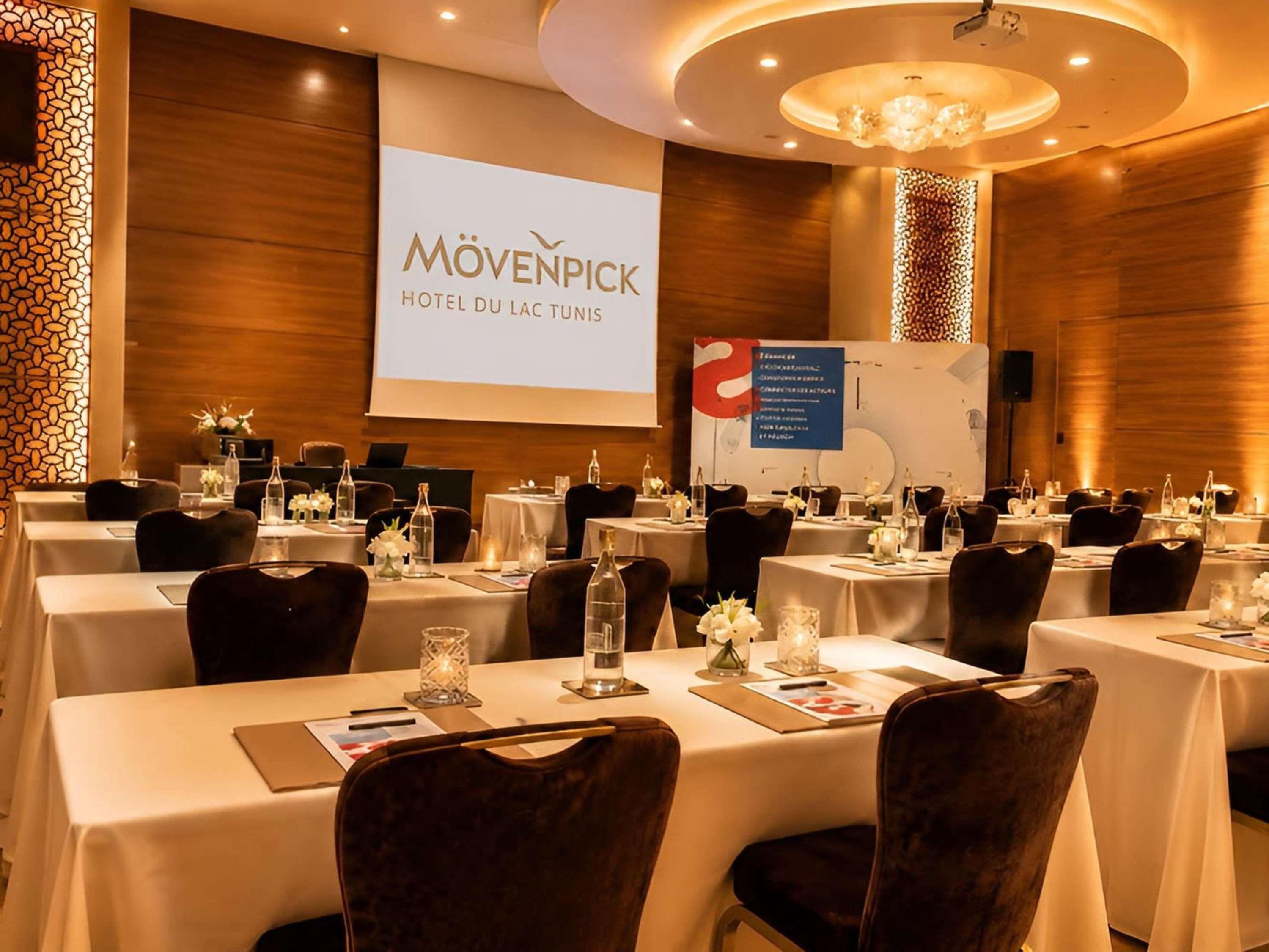 Une salle de conférence à l’hôtel Mövenpick du Lac Tunis, équipée de plusieurs tables, de chaises et d’un écran de présentation.