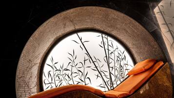 Una ventana circular con diseño de bambú, una silla acolchada y una pared con azulejos.