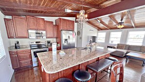 A spacious kitchen with granite countertops, wooden cabinets, and a central island with bar stools.