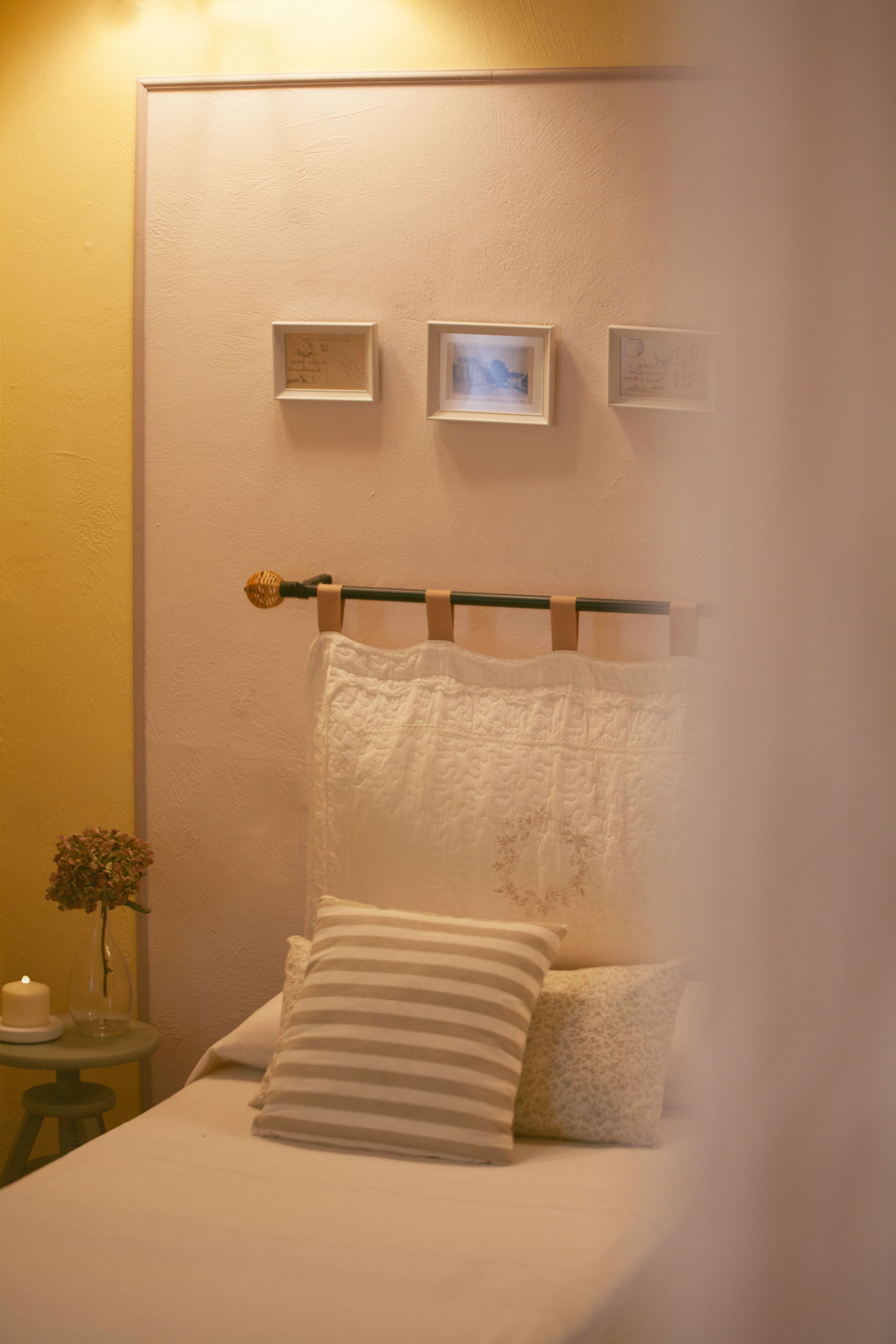 Un dormitorio con una cama, una mesita de noche con una vela y cuadros en la pared.