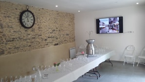 Une longue table dressée pour un repas, avec des verres à vin, un pichet en argent et une horloge au mur.