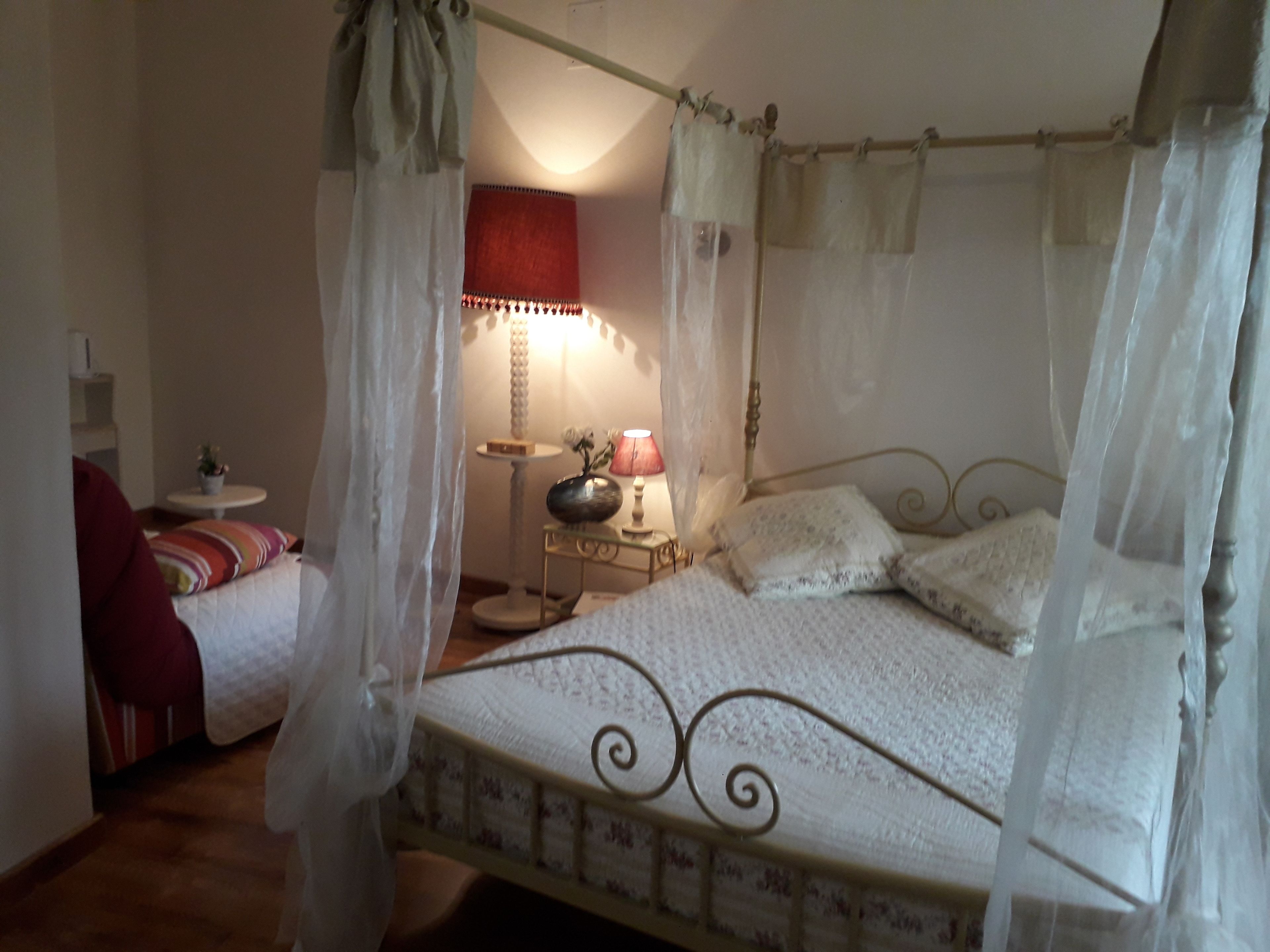 A bedroom with a four-poster bed, a bedside table with a lamp, and a chair.