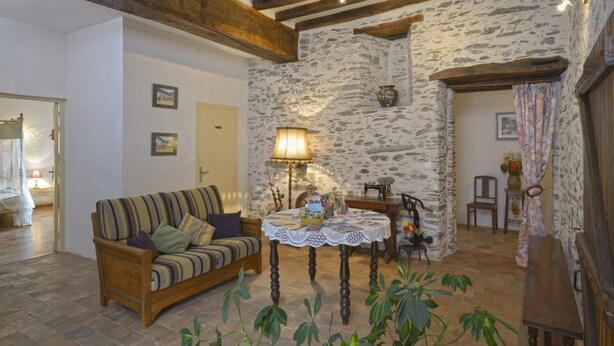 Un salon chaleureux avec un canapé en bois, une table recouverte d’une nappe en dentelle et un mur en pierre.