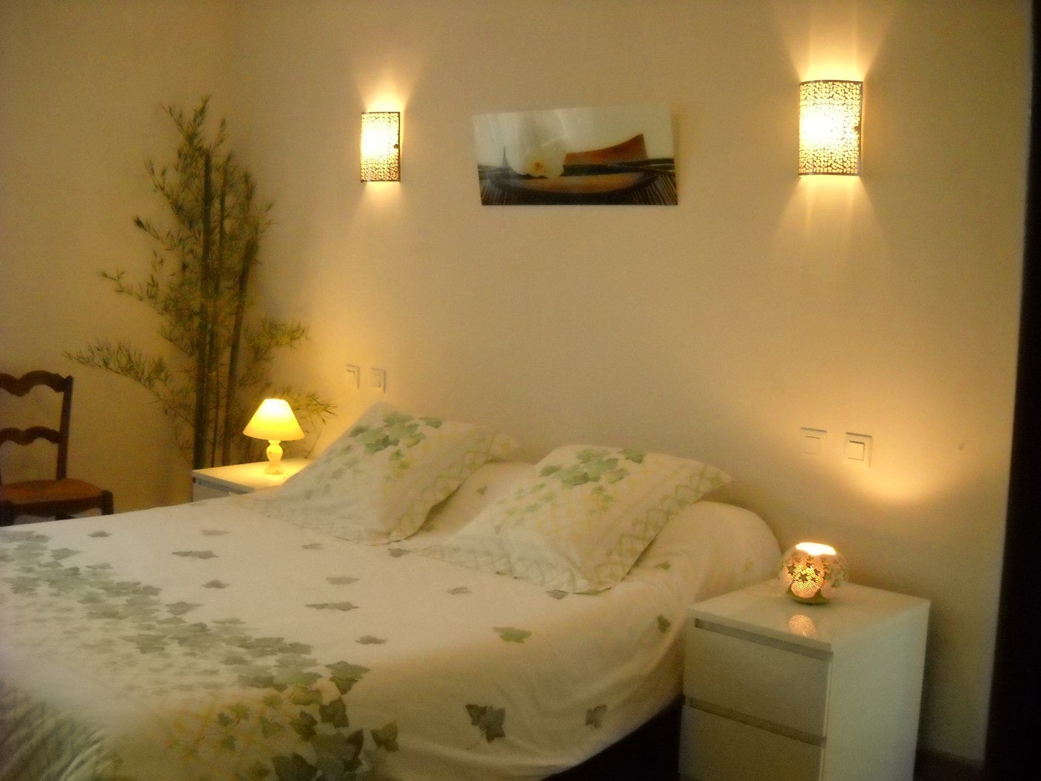 Un dormitorio con cama, lámparas de noche, mesita de noche y apliques de pared.
