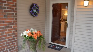 A house entrance with a brick wall, a welcome wreath, a flower arrangement, and a 'Home' mat.