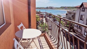 Varanda com mesa e cadeiras, vista para uma praia e estacionamento com carros.