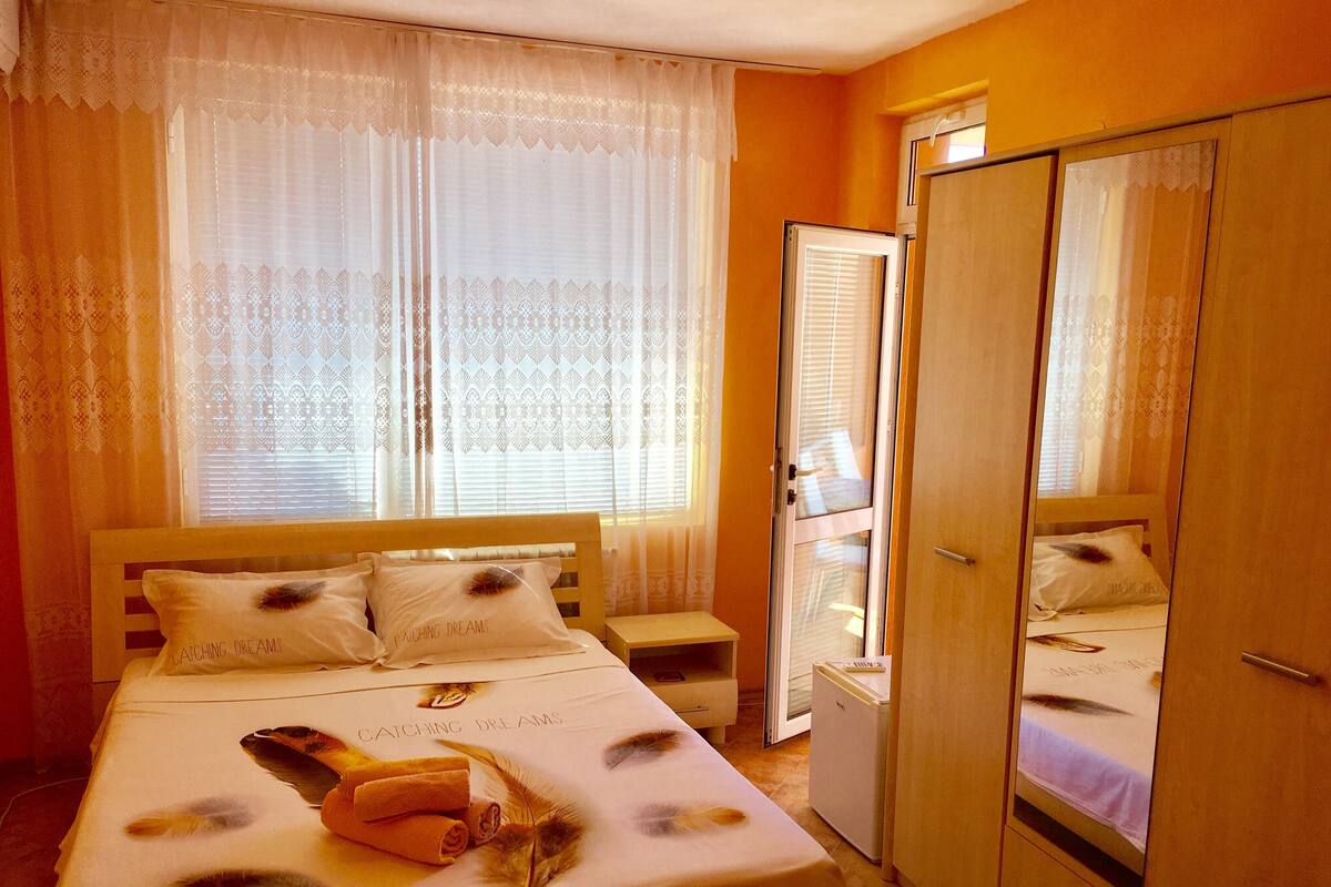 A bedroom with a bed, a wardrobe, a nightstand, and a window with curtains.