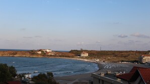 Vista costeira com edifícios perto da praia, céu claro e mar calmo.