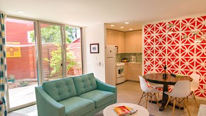 Ein modernes Wohnzimmer mit einem türkisfarbenen Sofa, einem runden Couchtisch und einem Essbereich mit einer rot gemusterten Wand und weißen Stühlen.