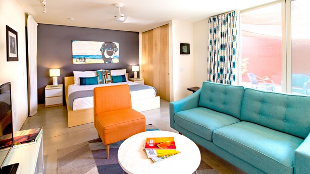 Ein modernes Hotelzimmer mit Bett, Sofa, Sessel, Couchtisch und großem Fenster mit Vorhängen.