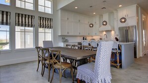A spacious kitchen with white cabinets, a large island, and a dining area with wooden chairs and a table.