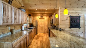 A wooden interior with a kitchen featuring granite countertops, wooden cabinets, and a central island.