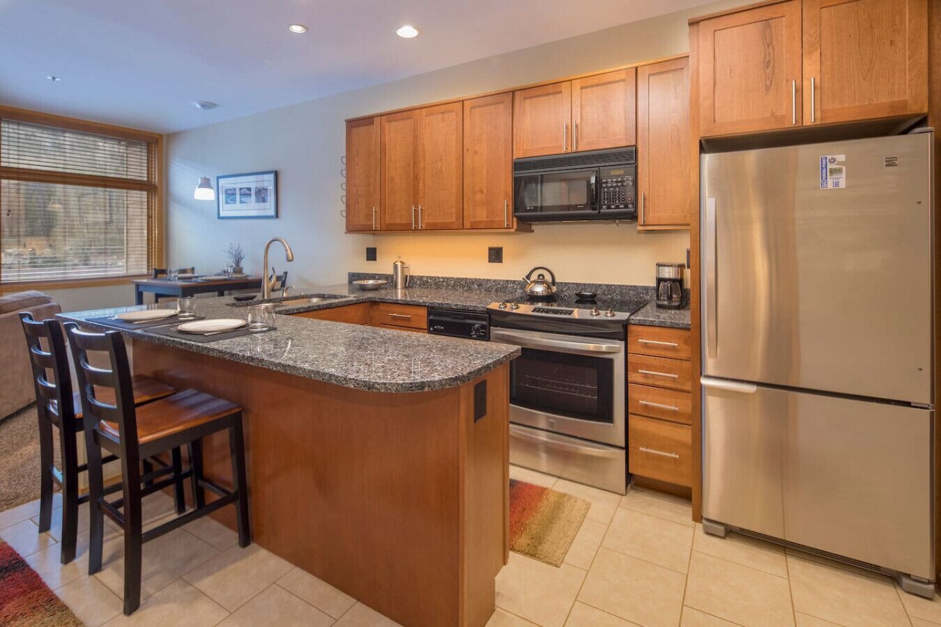 A modern kitchen with granite countertops, stainless steel appliances, wooden cabinets, and a large island with bar stools.