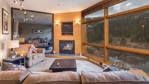 Un salon chaleureux avec une cheminée, des canapés en cuir et une grande fenêtre donnant sur un lac.