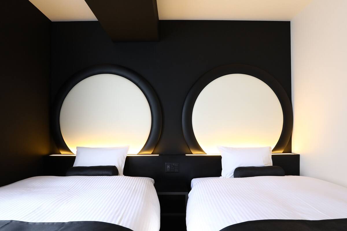 Une chambre d’hôtel avec deux lits, chacun surmonté d’un miroir rond.