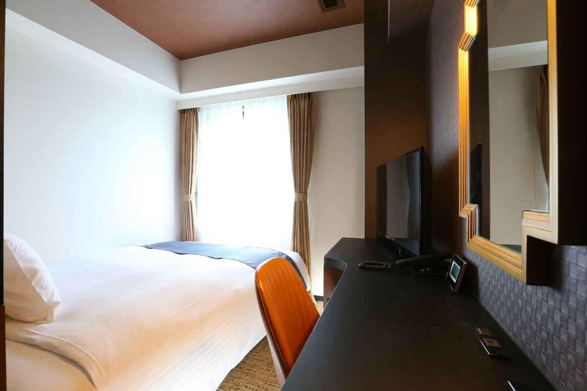 Une chambre d’hôtel équipée d’un lit, d’un bureau, d’une chaise, d’une télévision et d’un miroir.