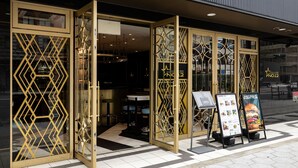 Een restaurantentree met een deur met geometrisch patroon, een menubord en een bord dat aangeeft dat het restaurant geopend is.