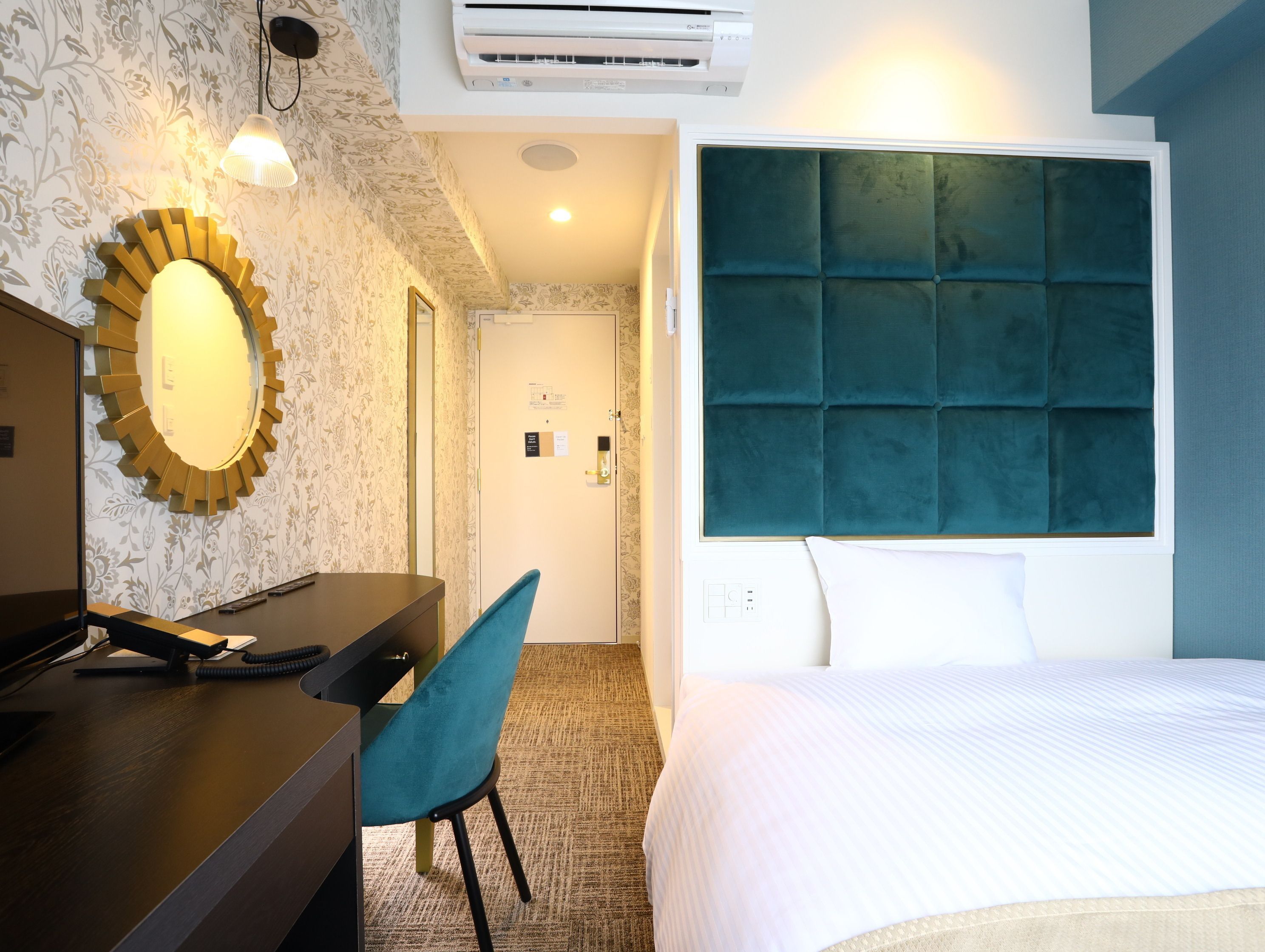 Une chambre d’hôtel comprenant un lit, un bureau avec un téléphone, une chaise, un miroir et un climatiseur fixé au mur.