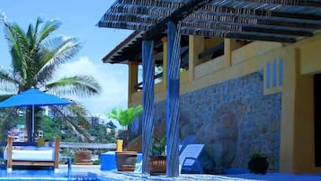 Uma área de piscina com deck de madeira, espreguiçadeiras e um espaço de estar coberto.