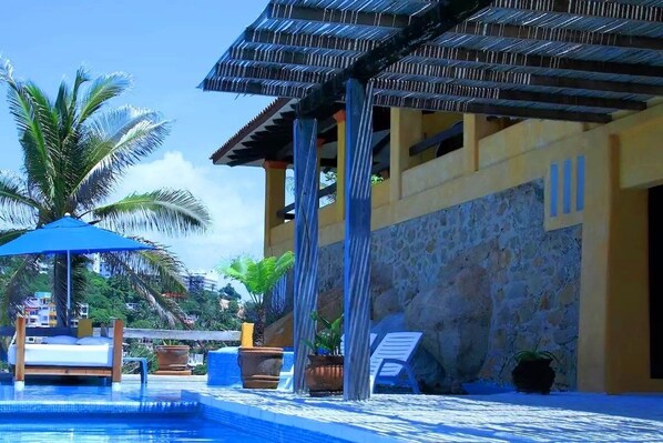 A pool area with a wooden deck, lounge chairs, and a covered seating area.