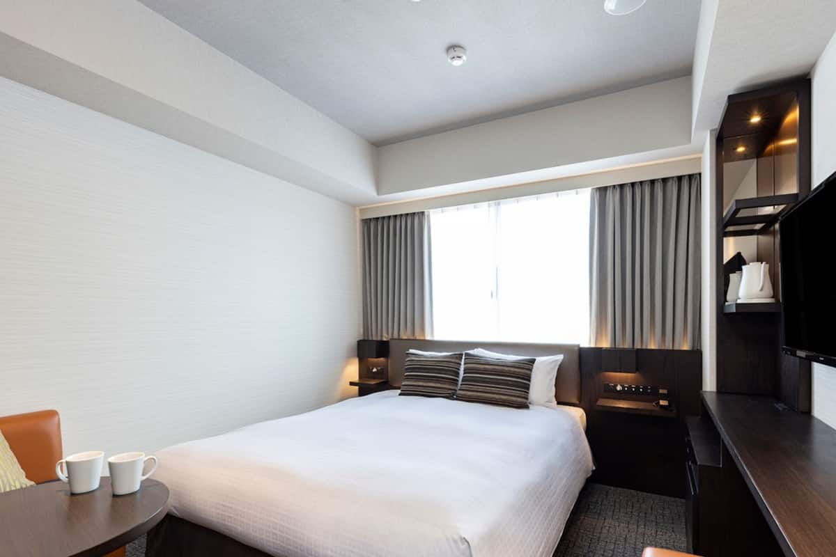 Une chambre d’hôtel avec un grand lit, un bureau, une chaise, une petite table avec deux tasses et un téléviseur posé sur un meuble.