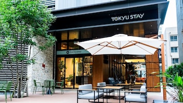Un espacio al aire libre con mesas y sillas frente a un edificio identificado como TOKYU STAY.
