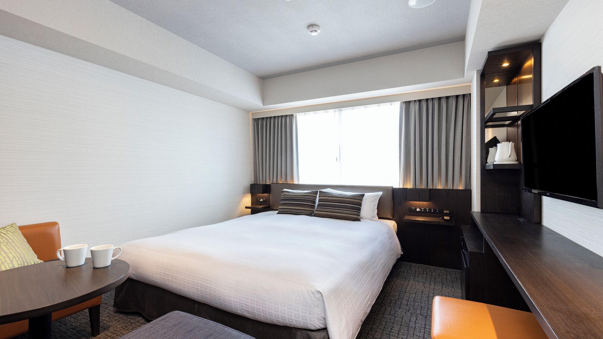 A hotel room with a bed, a desk, a chair, a TV, and a window with curtains.
