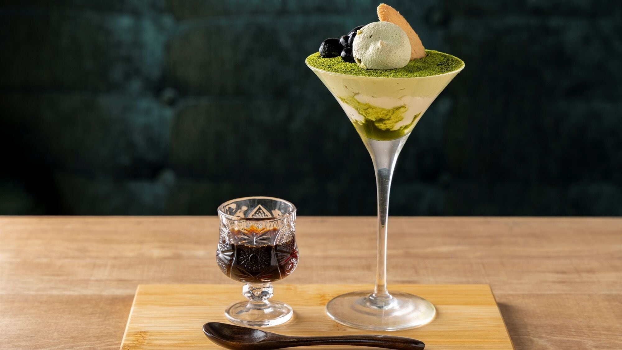 A martini glass with a layered drink and a scoop of ice cream on top, and a small glass with a dark liquid.
