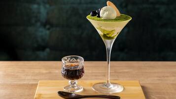 A martini glass with a layered drink and a scoop of ice cream on top, and a small glass with a dark liquid.