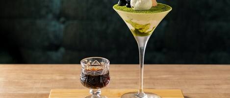 A martini glass with a layered drink and a scoop of ice cream on top, and a small glass with a dark liquid.
