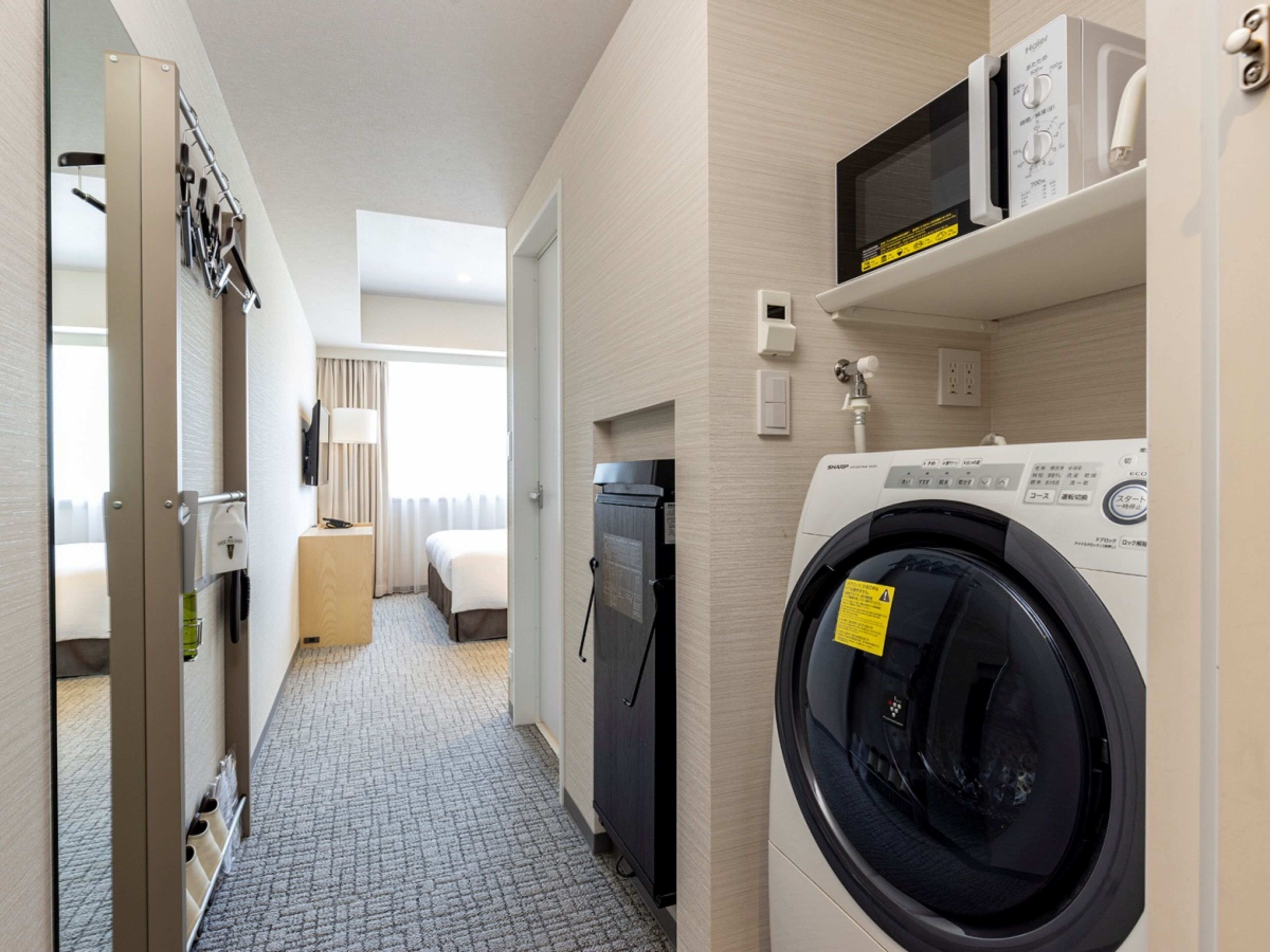 A hotel room with a washing machine, a microwave, a bed, a desk, and a bathroom.