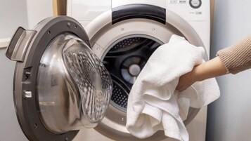A front-loading washing machine with a hand holding a white cloth in front of it.