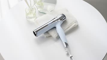 A hair dryer on a white surface with a towel and a glass container with a liquid.